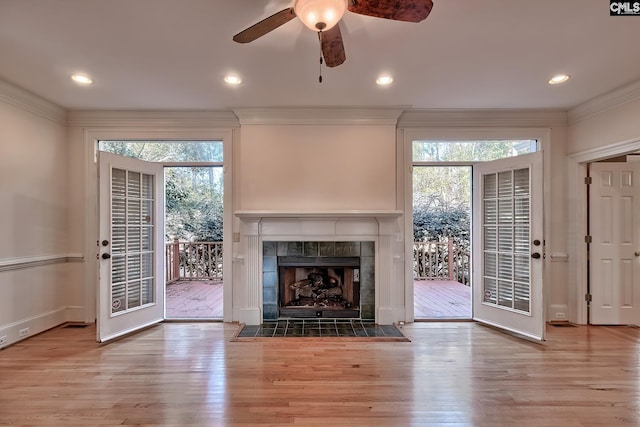 unfurnished living room with a tile fireplace, light wood-type flooring, ceiling fan, and a healthy amount of sunlight