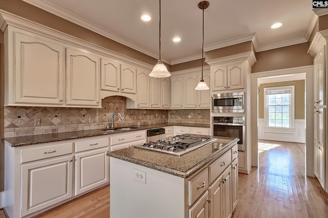 kitchen featuring appliances with stainless steel finishes, sink, decorative light fixtures, dark stone countertops, and a center island