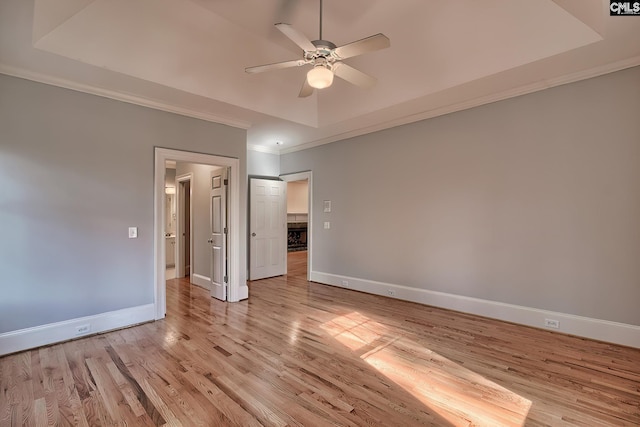 unfurnished bedroom featuring a raised ceiling, ceiling fan, light hardwood / wood-style flooring, and ornamental molding