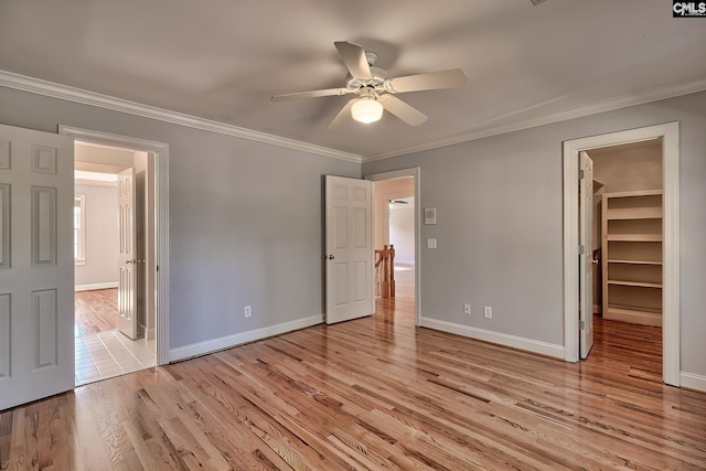 unfurnished bedroom featuring a walk in closet, ceiling fan, crown molding, and light hardwood / wood-style flooring