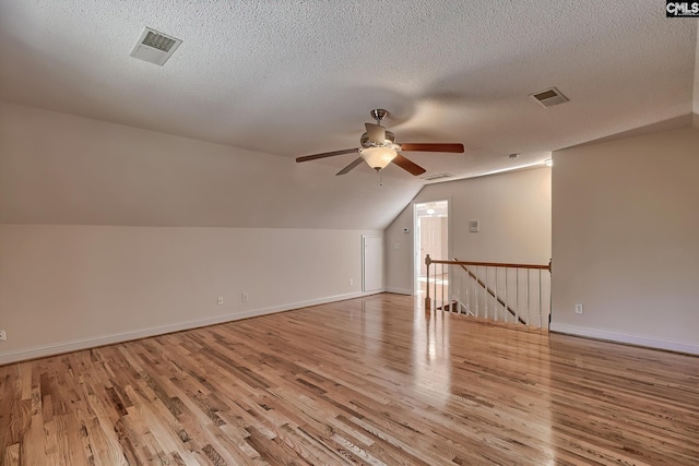 additional living space featuring a textured ceiling, light hardwood / wood-style flooring, vaulted ceiling, and ceiling fan