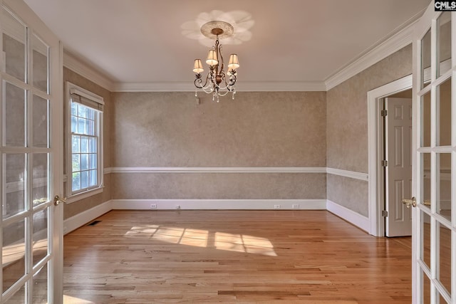 spare room featuring crown molding, french doors, light wood-type flooring, and a notable chandelier