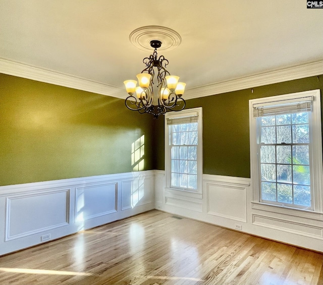 unfurnished dining area featuring crown molding, light wood-type flooring, and an inviting chandelier