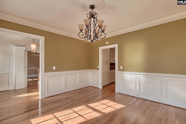 spare room with ornamental molding, light wood-type flooring, and a notable chandelier