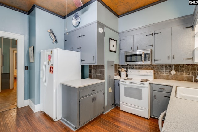 kitchen with crown molding, white appliances, backsplash, and dark wood-type flooring