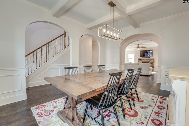 dining room featuring coffered ceiling, ceiling fan with notable chandelier, a stone fireplace, dark hardwood / wood-style floors, and beamed ceiling