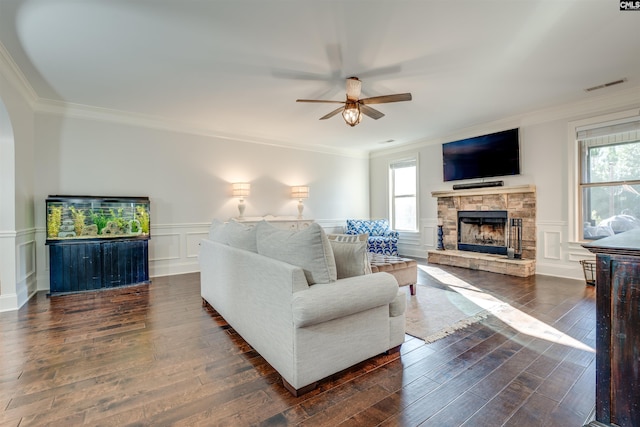 living room with dark hardwood / wood-style floors, a stone fireplace, plenty of natural light, and ornamental molding