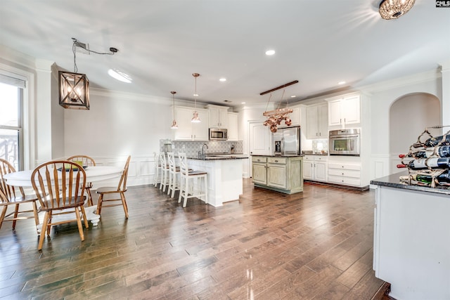 kitchen featuring stainless steel appliances, a kitchen island, decorative light fixtures, a kitchen bar, and white cabinets