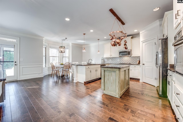 kitchen featuring appliances with stainless steel finishes, a kitchen island, hanging light fixtures, and ornamental molding