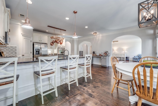 kitchen with a breakfast bar, dark stone counters, white cabinets, appliances with stainless steel finishes, and decorative light fixtures