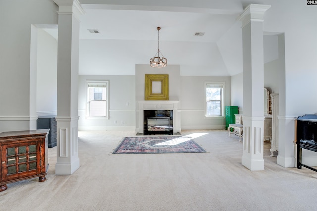 carpeted living room with decorative columns, vaulted ceiling, and a notable chandelier