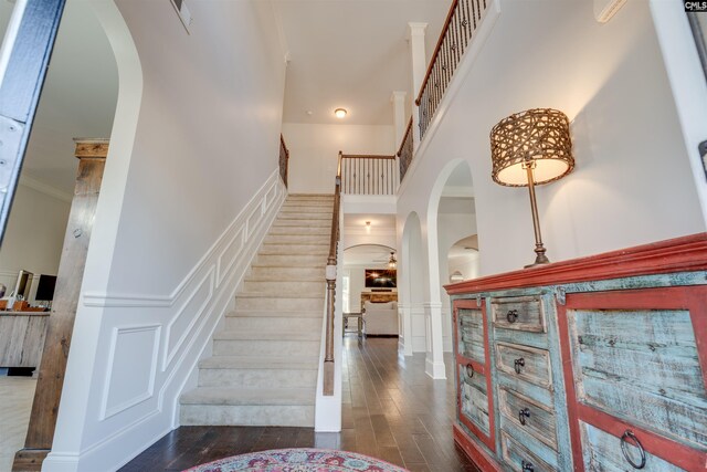 stairway with a towering ceiling, hardwood / wood-style flooring, and ornamental molding