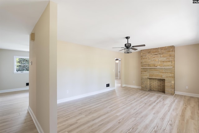 unfurnished living room with light hardwood / wood-style floors, a stone fireplace, and ceiling fan