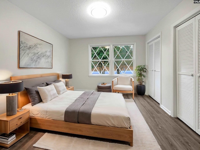 bedroom featuring two closets, a textured ceiling, and dark hardwood / wood-style floors