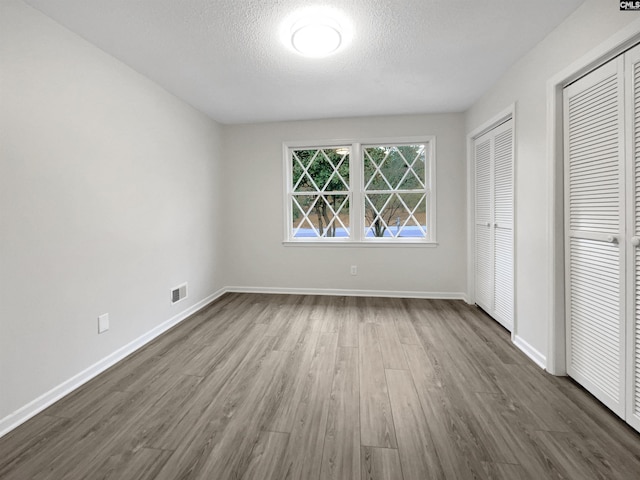 unfurnished bedroom with a textured ceiling, multiple closets, and dark hardwood / wood-style floors