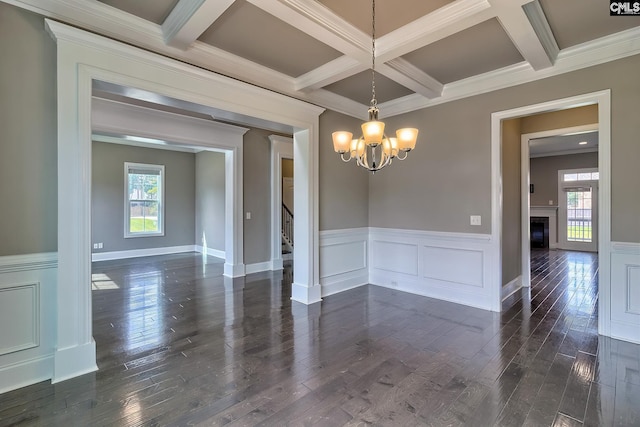 empty room featuring ornamental molding, coffered ceiling, dark wood-type flooring, an inviting chandelier, and beamed ceiling