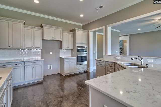 kitchen with backsplash, light stone counters, sink, and stainless steel double oven