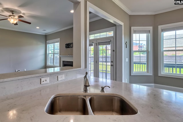 kitchen featuring light stone counters, sink, ceiling fan, and ornamental molding