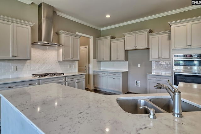 kitchen with light stone countertops, stainless steel appliances, wall chimney exhaust hood, and sink