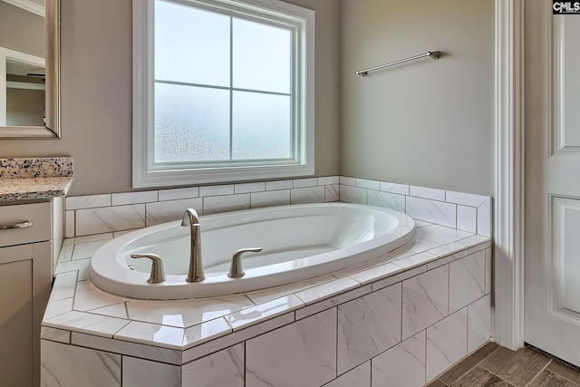 bathroom with vanity, a relaxing tiled tub, and a healthy amount of sunlight