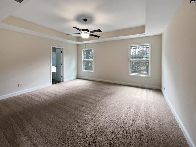 empty room featuring a tray ceiling, ceiling fan, and carpet floors