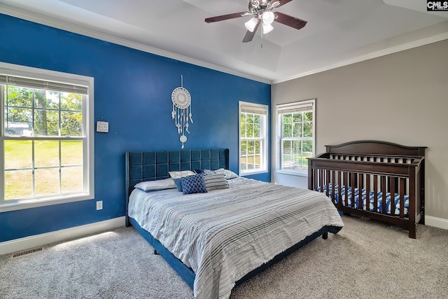 carpeted bedroom with a tray ceiling, multiple windows, ceiling fan, and crown molding