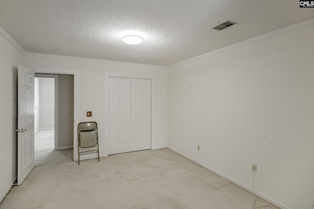 unfurnished bedroom with a closet, light colored carpet, a textured ceiling, and ornamental molding