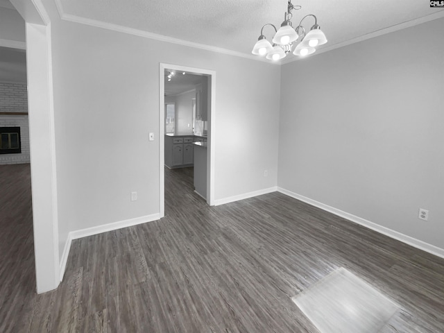 spare room featuring an inviting chandelier, dark hardwood / wood-style floors, a textured ceiling, a fireplace, and ornamental molding