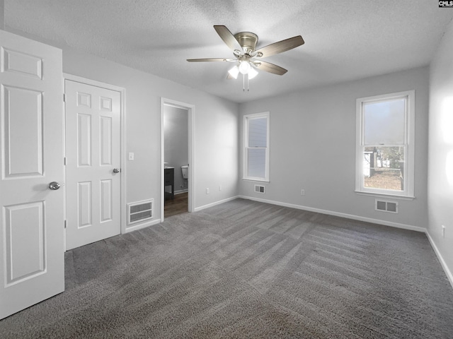 unfurnished bedroom featuring a textured ceiling, ensuite bathroom, dark carpet, and ceiling fan