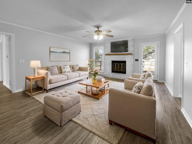 living room with ceiling fan, dark wood-type flooring, a brick fireplace, crown molding, and a textured ceiling