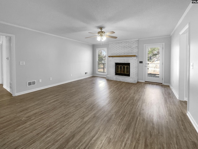 unfurnished living room with a brick fireplace, a textured ceiling, ceiling fan, crown molding, and dark hardwood / wood-style floors