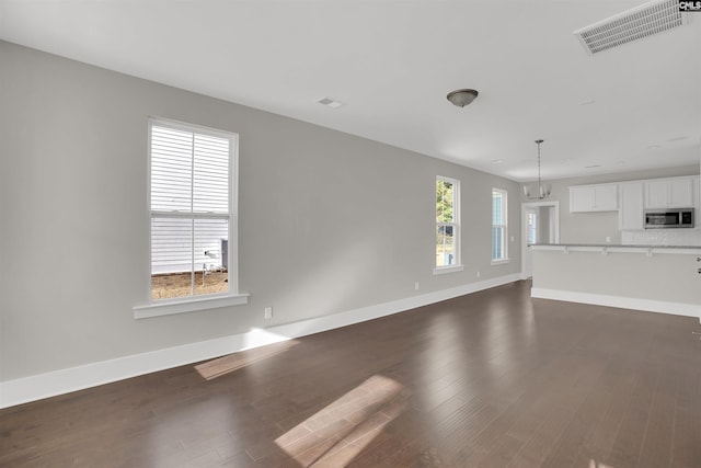 unfurnished living room with plenty of natural light, dark hardwood / wood-style floors, and a chandelier