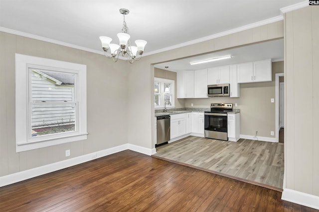 kitchen featuring white cabinets, hanging light fixtures, ornamental molding, appliances with stainless steel finishes, and a chandelier