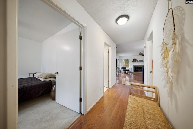 corridor with vaulted ceiling, a textured ceiling, and light hardwood / wood-style flooring