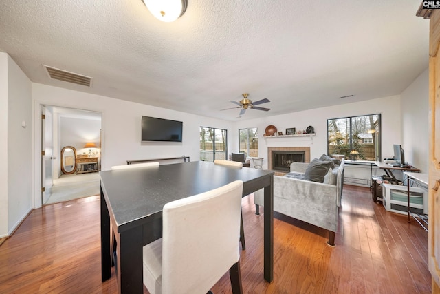 dining space with ceiling fan, a textured ceiling, a tile fireplace, and dark wood-type flooring