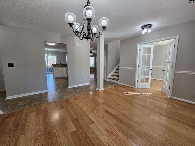 unfurnished dining area with ceiling fan with notable chandelier, hardwood / wood-style floors, a textured ceiling, and french doors