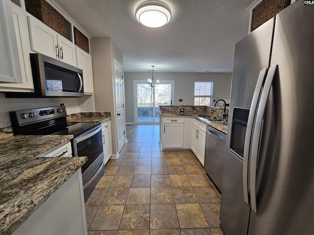 kitchen with white cabinets, appliances with stainless steel finishes, an inviting chandelier, sink, and hanging light fixtures