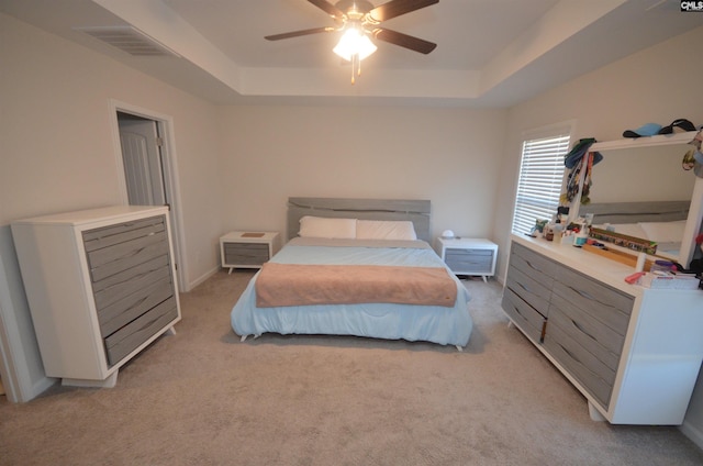 bedroom with ceiling fan, light carpet, and a tray ceiling