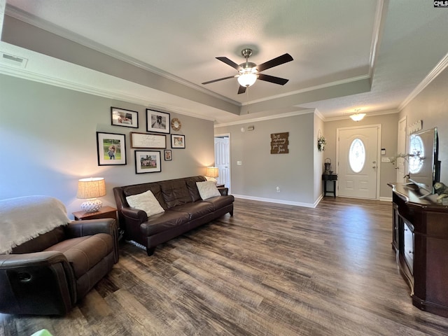 living room with a tray ceiling, crown molding, ceiling fan, and dark wood-type flooring