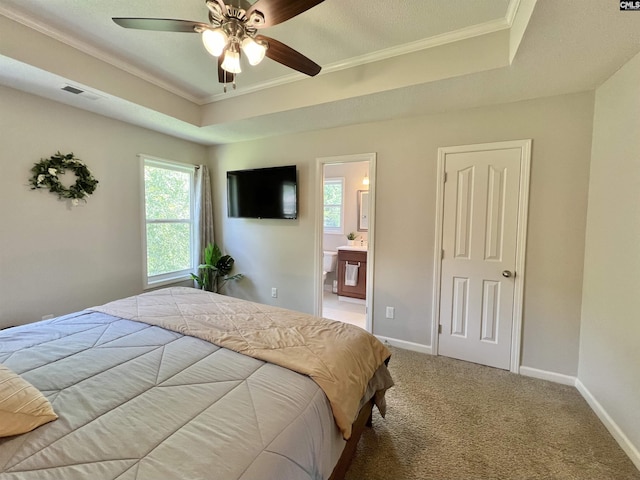 carpeted bedroom featuring a tray ceiling, connected bathroom, ceiling fan, and crown molding