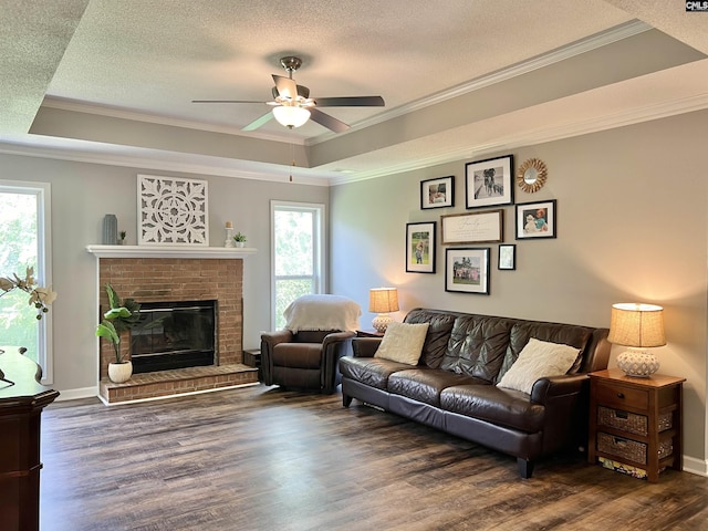 living room with dark hardwood / wood-style flooring, a tray ceiling, a brick fireplace, and ceiling fan