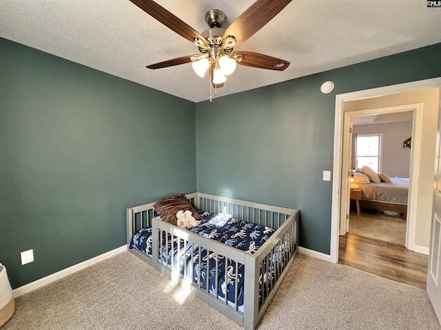 bedroom with carpet flooring, ceiling fan, a nursery area, and a textured ceiling