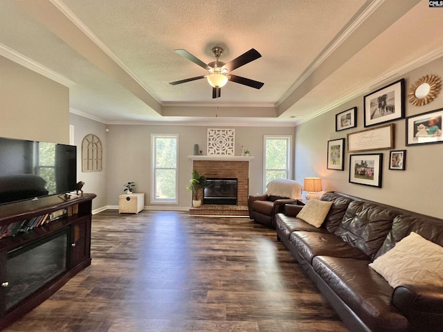 living room featuring dark hardwood / wood-style floors, a healthy amount of sunlight, a tray ceiling, and a brick fireplace