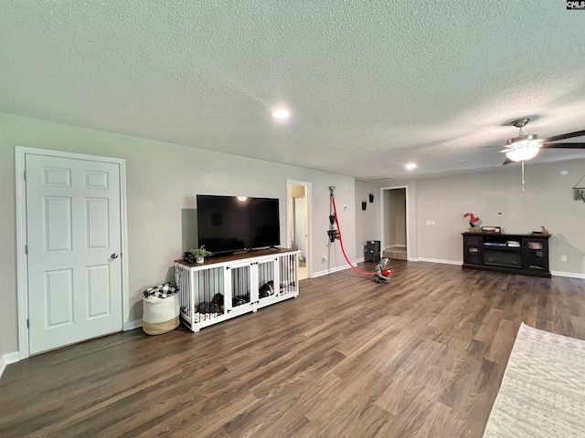 living room featuring ceiling fan, dark wood-type flooring, and a textured ceiling