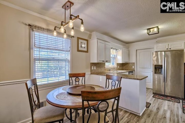 dining room featuring a wealth of natural light, light hardwood / wood-style floors, a textured ceiling, and ornamental molding