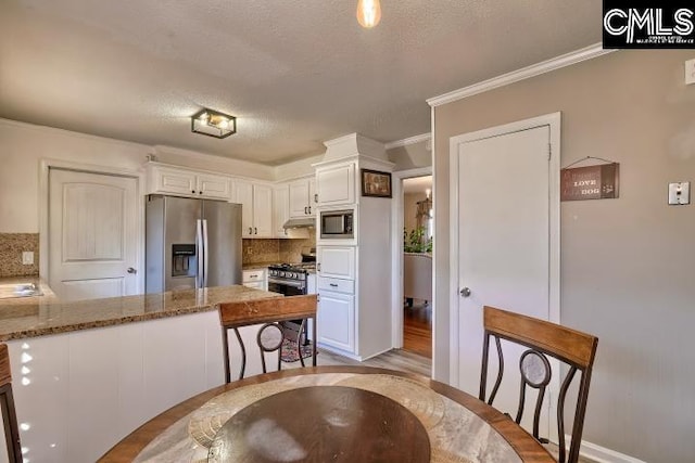 kitchen featuring white cabinetry, light stone countertops, backsplash, kitchen peninsula, and appliances with stainless steel finishes