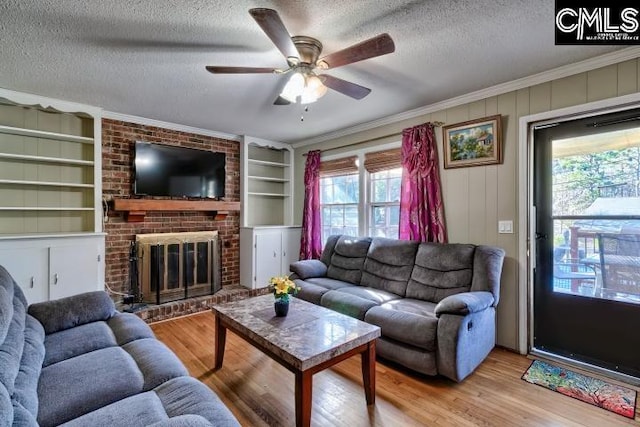 living room featuring built in shelves, a textured ceiling, crown molding, light hardwood / wood-style flooring, and a fireplace