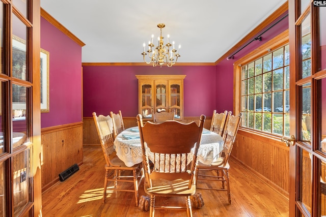 dining area with a chandelier, wooden walls, light wood-type flooring, and ornamental molding