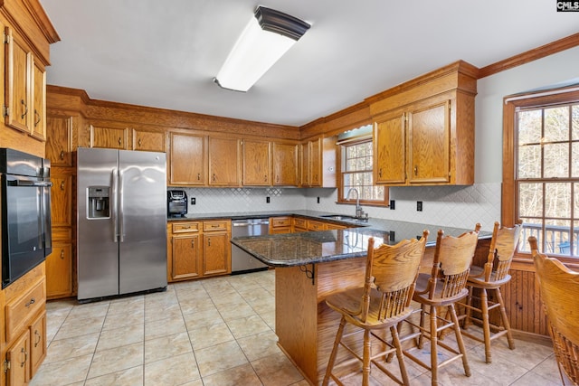 kitchen with sink, stainless steel appliances, kitchen peninsula, dark stone countertops, and a breakfast bar