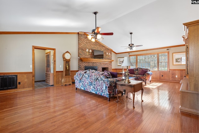 living room featuring hardwood / wood-style floors, lofted ceiling, crown molding, ceiling fan, and a fireplace